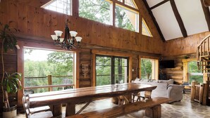 L’intérieur d’un chalet rustique est agrémenté d’une grande table à manger en bois, de bancs, d’un canapé et d’un téléviseur fixé au mur.