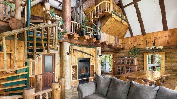 L’intérieur d’une cabane en rondins, avec une cheminée, un escalier en bois et un coin repas.
