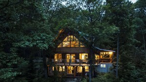 Une cabane avec un escalier en pierre menant à une terrasse, le tout entouré d’une forêt dense.
