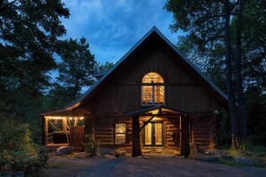 A log cabin with a large central window, a porch with lights, and a rustic exterior.