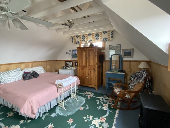 A bedroom with a bed, dresser, vanity, rocking chair, and a ceiling fan.