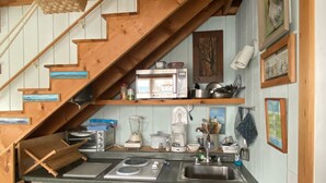 A compact kitchen with a wooden staircase, a built-in refrigerator, a sink, and various appliances.