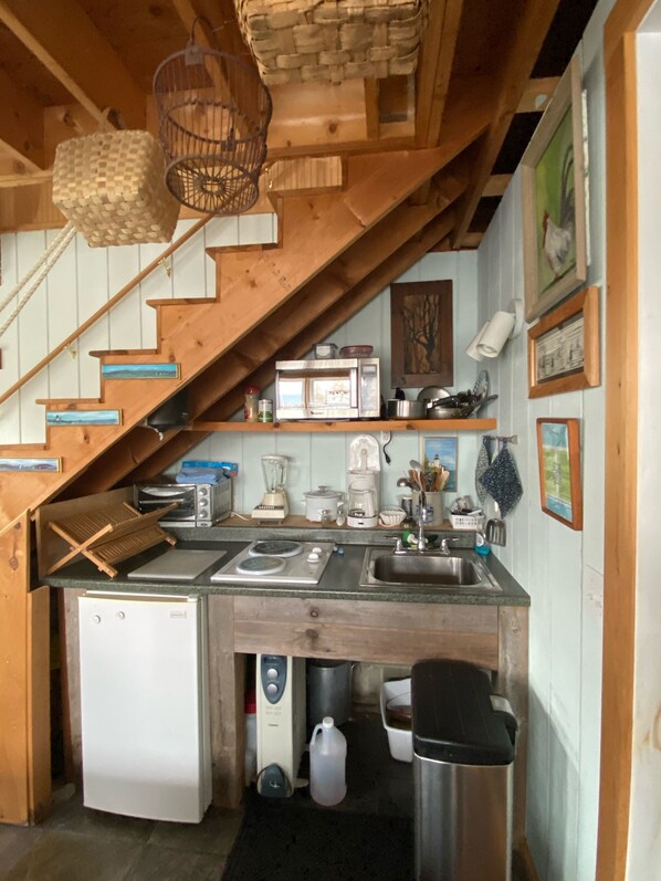 A compact kitchen with a wooden staircase, a built-in refrigerator, a sink, and various appliances. - Acadia Stones Throw Cottage (Southwest Harbor)