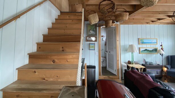 A wooden staircase leading to a room with a view of the sea, a sofa, and a lamp.