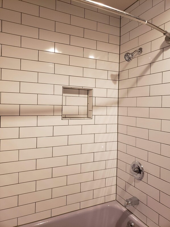 Een badkamer met witte metrotegels, een rechthoekige spiegel, een douche met handdouche en een bad met kraan.