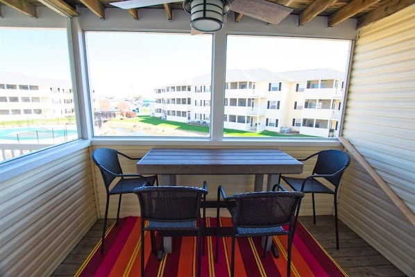 A balcony with a table and chairs, a view of buildings, and a red striped rug.