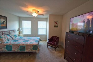 A bedroom with a bed, a chair, a dresser, a ceiling fan, and a TV.