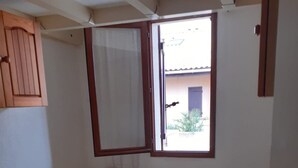 A small bedroom with a single bed, a window, a wooden cabinet, and a small table.