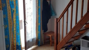 A small, cozy room with a bed, a chair, a wooden staircase, and a window with curtains.