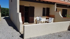 A small building with a gravel driveway, a table with chairs, and a bag on the table.