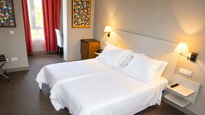 Habitación de hotel con cama doble, dos mesitas de noche con lámparas, un escritorio con silla, un armario y un cuadro en la pared.