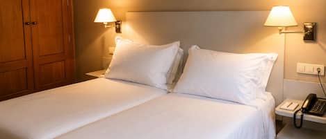 Una habitación de hotel con una cama doble, dos lámparas de noche, un teléfono en la mesita y un armario de madera.