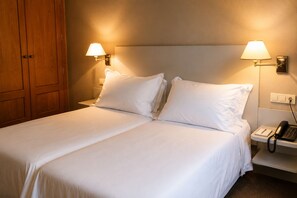 Een hotelkamer met een tweepersoonsbed, twee bedlampen, een bedtelefoon en een houten garderobe.