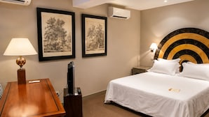 Habitación de hotel con cama, escritorio, lámpara, televisor y cuadros en la pared.