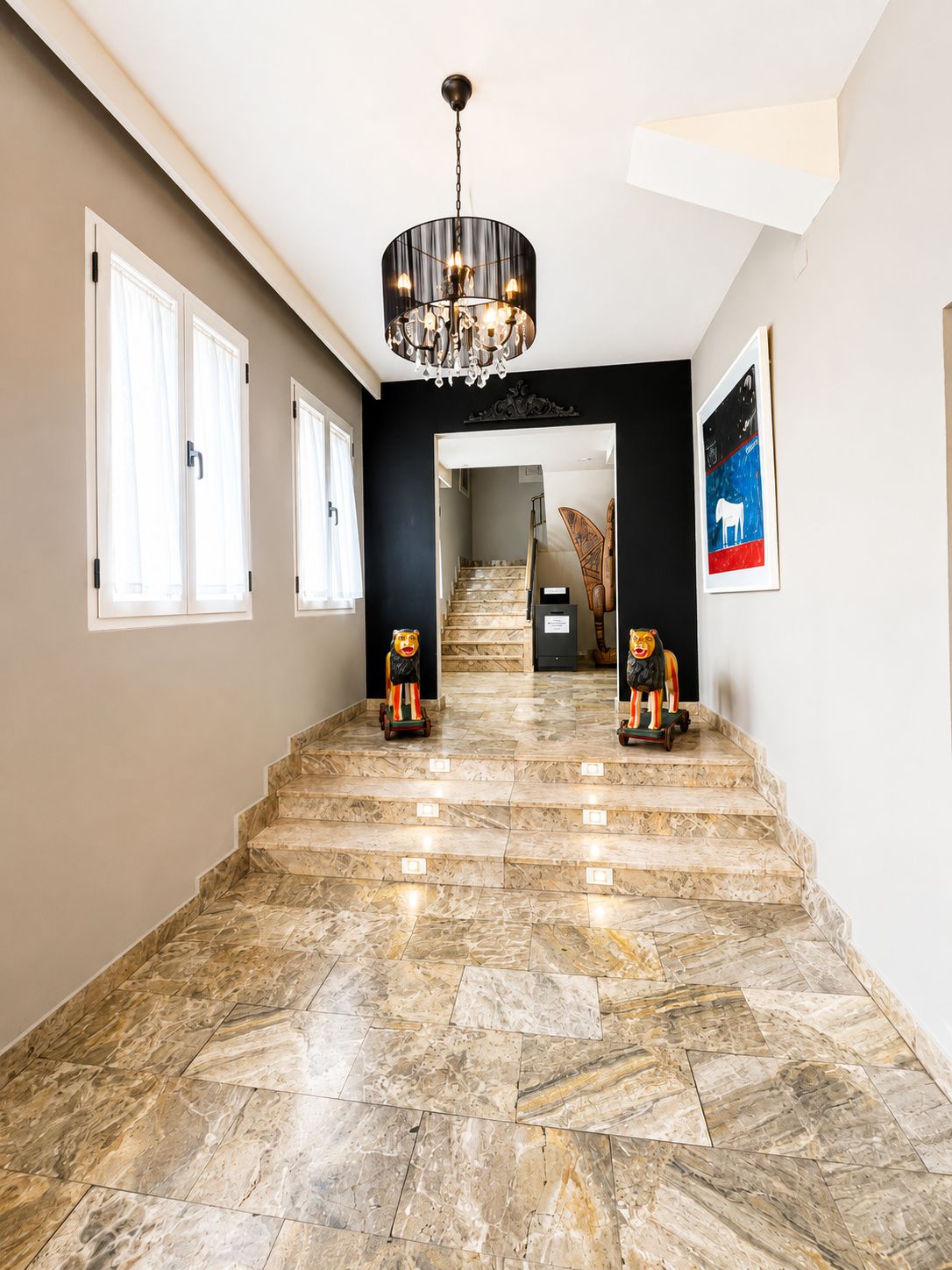 Una imponente escalera con suelo de mármol que conduce a un segundo piso, un candelabro y una obra de arte enmarcada en la pared.