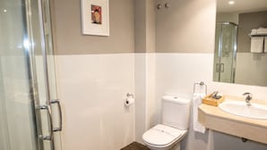Un baño moderno con cabina de ducha de vidrio, inodoro y lavamanos con espejo.