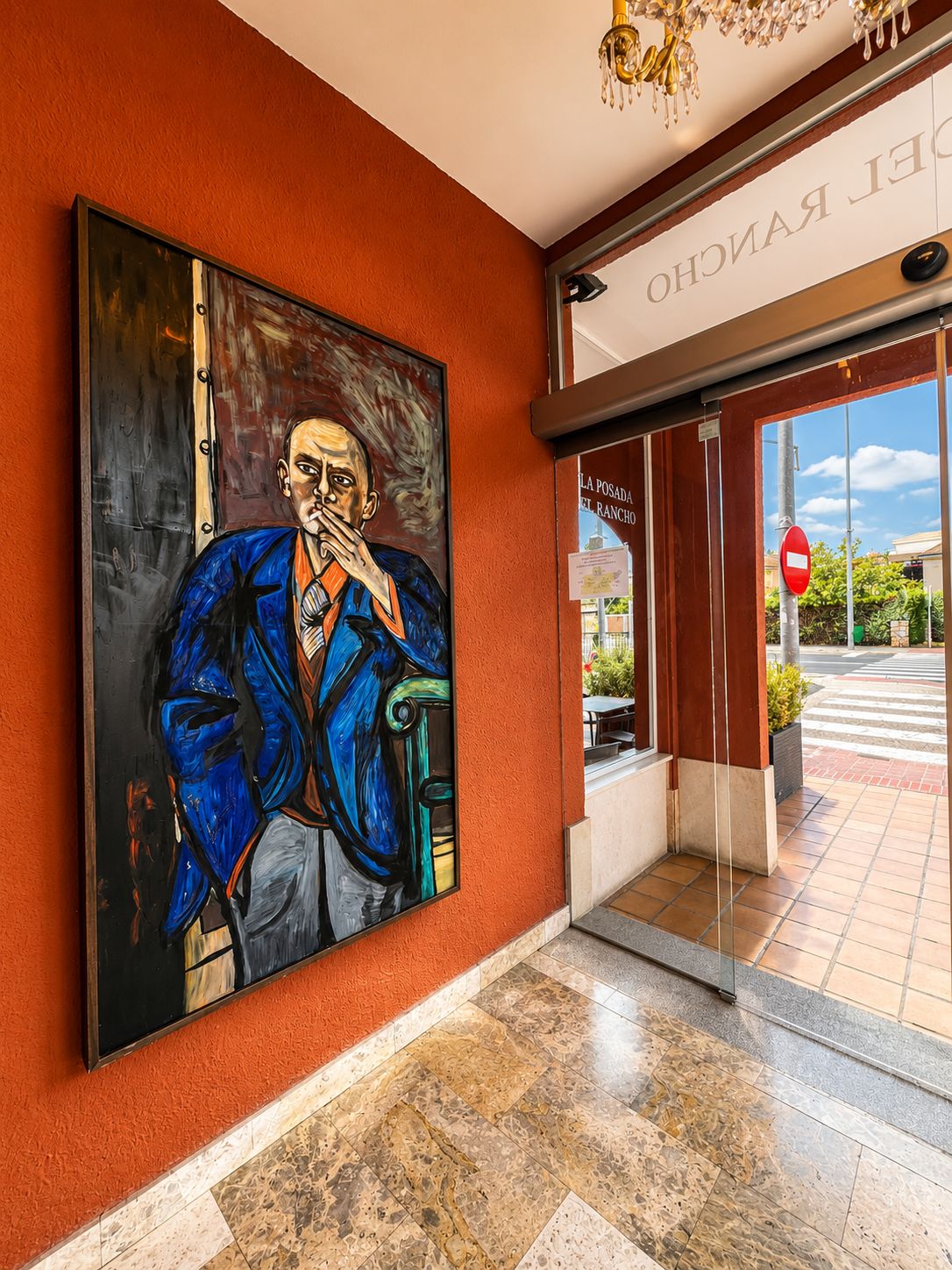 A hotel entrance with a large mural, a chandelier, and a glass door with a red 'no entry' sign.