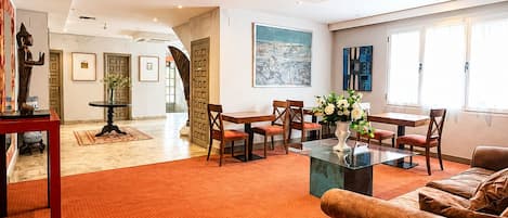A spacious living area with a red carpet, a sofa, a dining table with chairs, and artwork on the walls.
