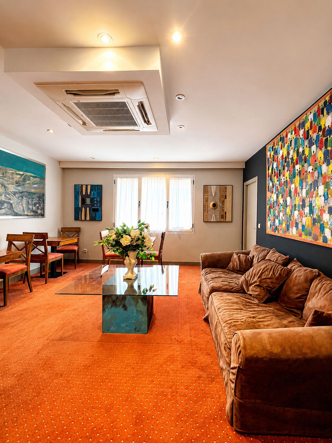 Een moderne woonkamer met een glazen salontafel, een bruine leren bank en een kleurrijk abstract schilderij aan de muur.