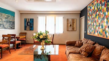Een moderne woonkamer met een glazen salontafel, een bruine leren bank en een kleurrijk abstract schilderij aan de muur.