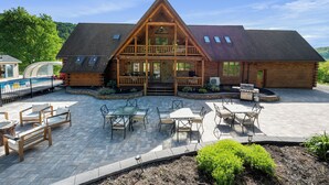 A log cabin with a balcony, outdoor seating, and a stone patio. - Indoor Pool, Giant Game Room Party Lodge, Entire Estate Rental  (Hancock)