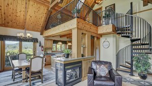 A spacious living area with a fireplace, a dining table, and a leather sofa. A wooden staircase connects the two floors. - Indoor Pool, Giant Game Room Party Lodge, Entire Estate Rental  (Hancock)