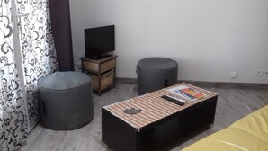 A small room with a television on a wooden stand, two grey bean bag chairs, a small table with a remote control and books, and a patterned curtain. - Nice Appart T3 duplex 4pers-Clim- 5mn from the Port Ostréicole de la Teste de Buch (La Teste-de-Buch)