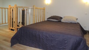 A bedroom with a wooden bed frame, a dark-colored bedspread, and two pillows. There is a small wooden structure in the corner, possibly a storage unit or a playpen. - Nice Appart T3 duplex 4pers-Clim- 5mn from the Port Ostréicole de la Teste de Buch (La Teste-de-Buch)