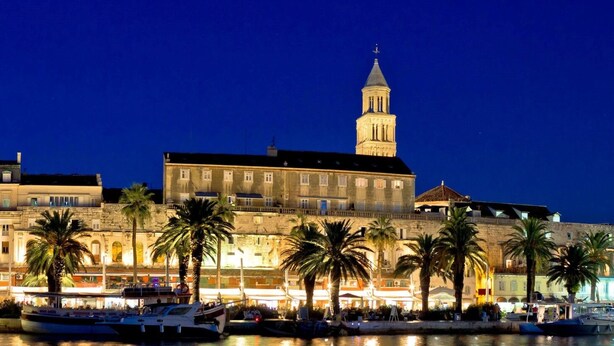 A waterfront hotel with multiple buildings, including a prominent tower, and several boats docked in the marina.