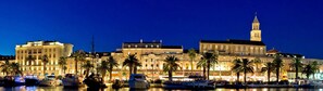 Un hotel sul lungomare con diversi edifici, tra cui una torre imponente, e alcune imbarcazioni ormeggiate nel porto turistico.