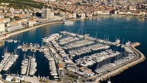 An aerial view of a marina with numerous boats docked, surrounded by a cityscape and mountains in the background.