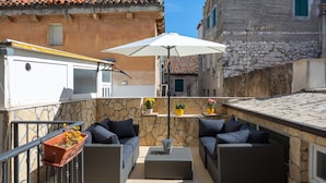 An outdoor patio with wicker furniture, a white umbrella, and potted plants.