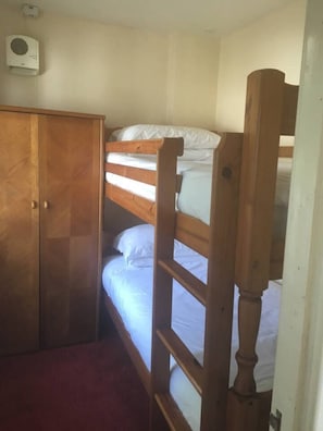 A bunk bed with white bedding, a wooden wardrobe, and a ceiling-mounted air conditioning unit.