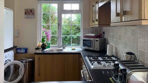 A kitchen with wooden cabinets, a gas stove, a microwave, and a window with a view of greenery.