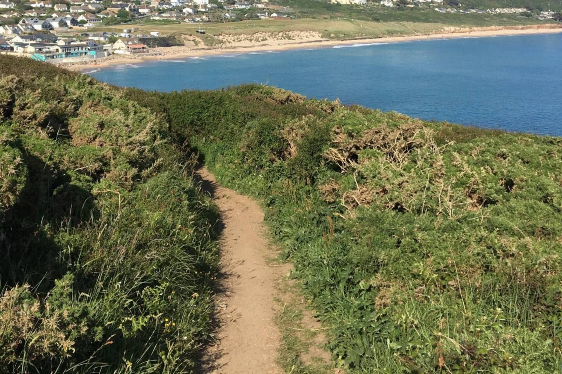 A coastal path with a view of a beach and houses in the distance.