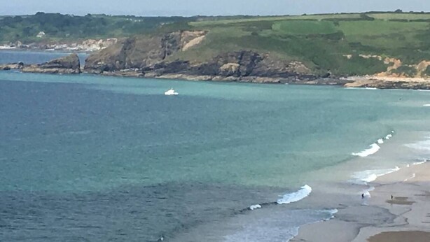 A coastal landscape with a beach, rocky cliffs, and a boat in the water.