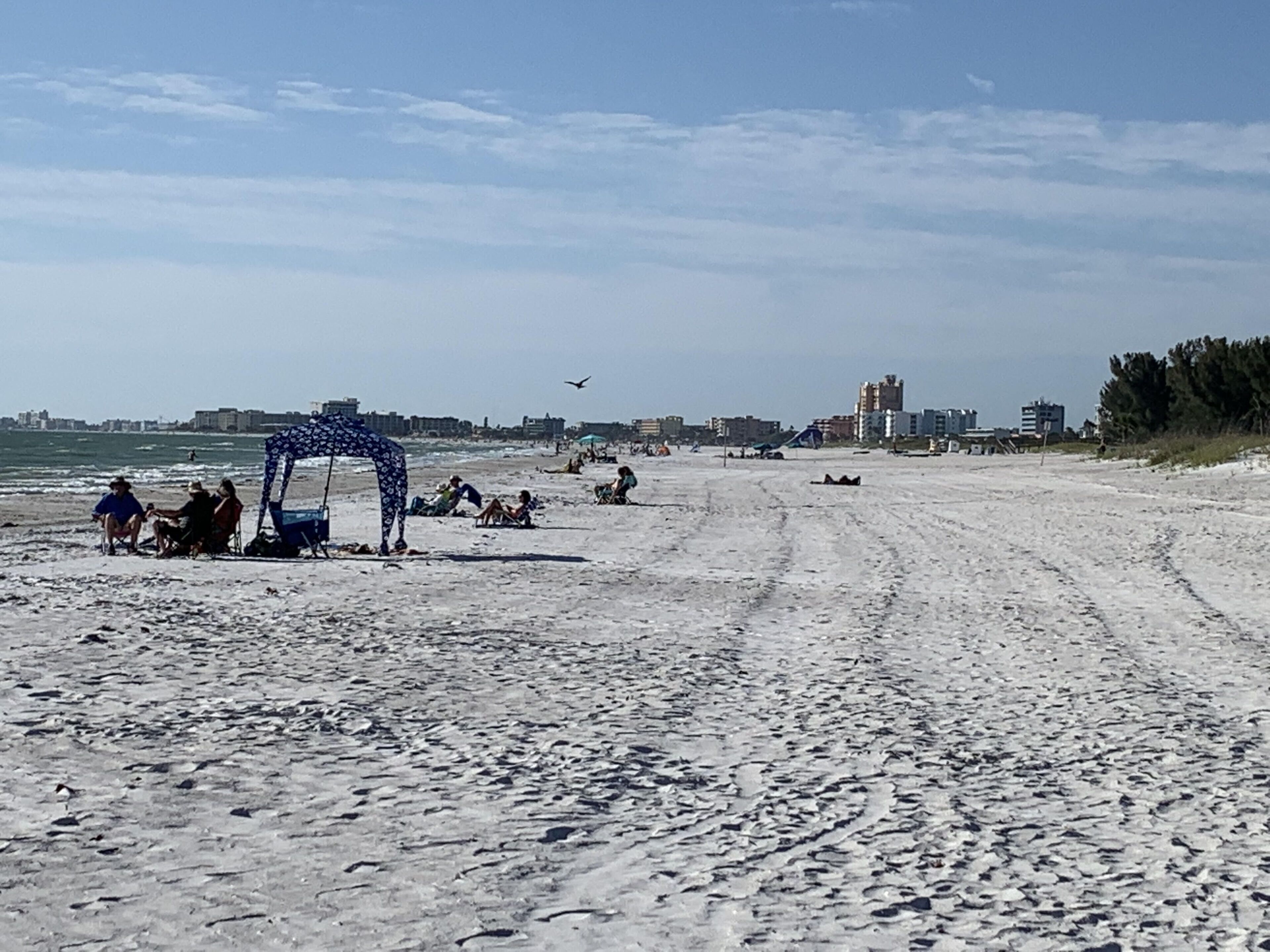 En sandstrand med en paviljong, människor som kopplar av och byggnader i bakgrunden.
