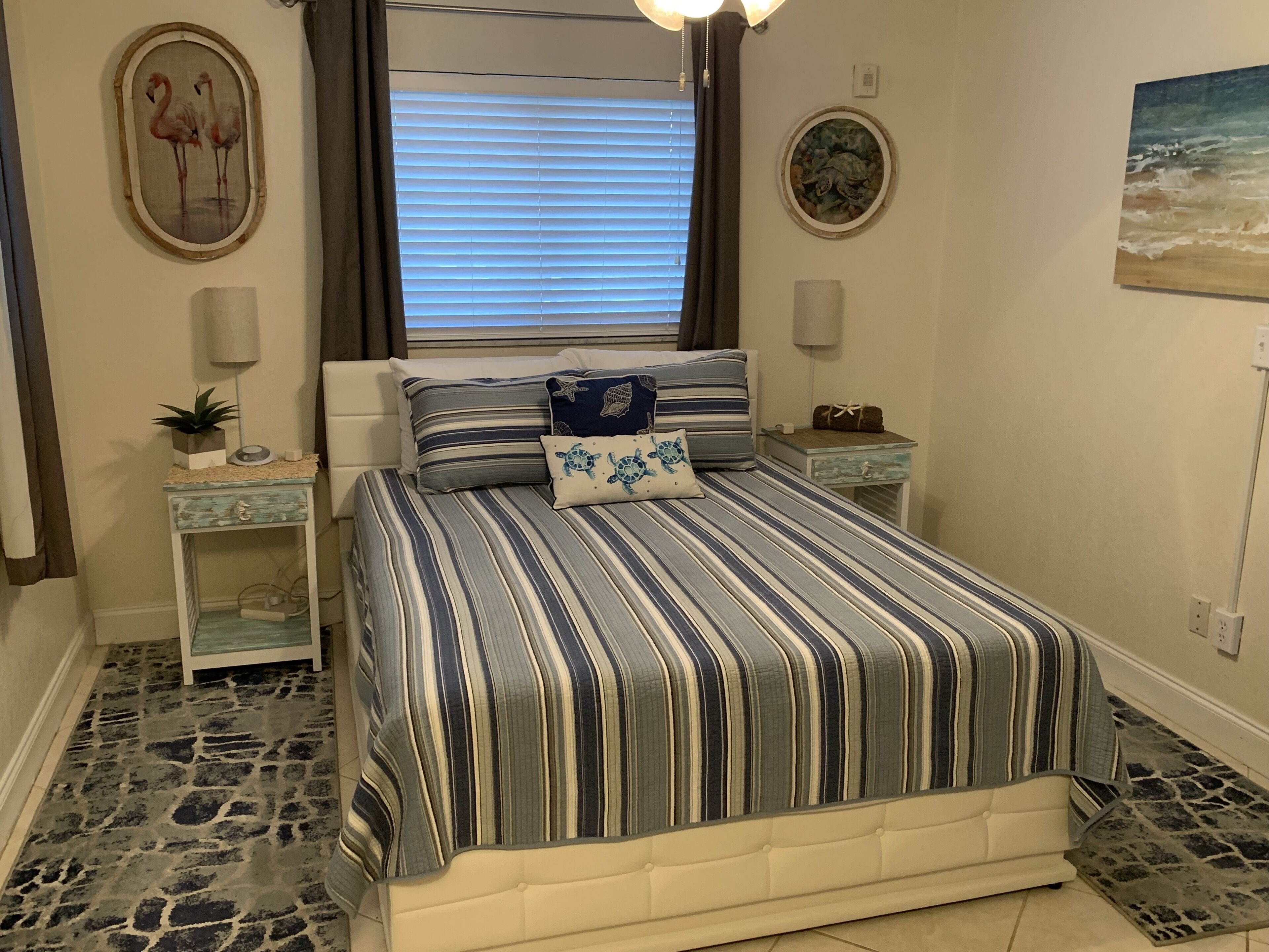 A bedroom with a striped bedspread, a headboard, bedside tables, and wall art.