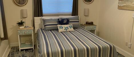 A bedroom with a striped bedspread, a headboard, bedside tables, and wall art.