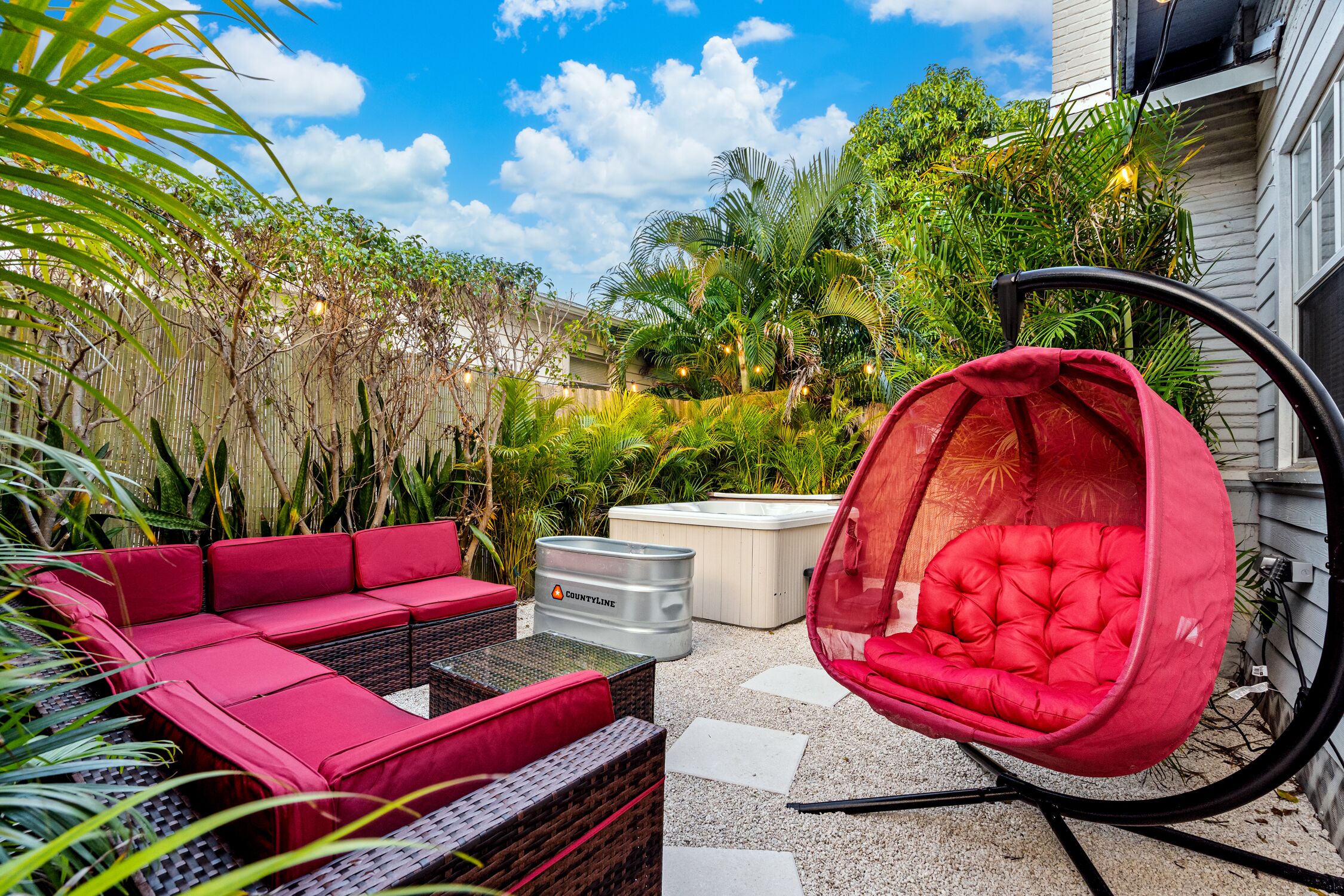 A patio with a red sofa, a hanging chair, and a hot tub.