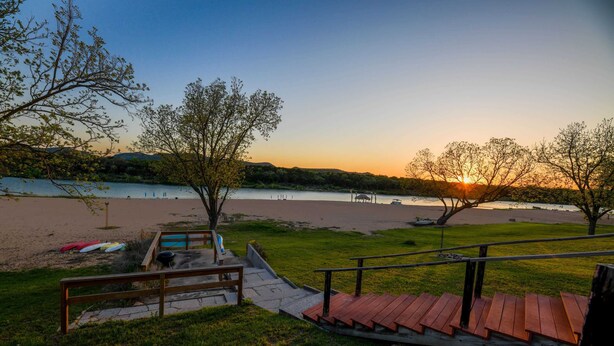 Un parc au bord de la rivière, doté d’une terrasse en bois, de tables de pique-nique et offrant une vue sur le coucher de soleil sur l’eau.