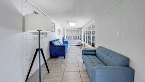 Un salon moderne avec un canapé bleu, un fauteuil bleu, une lampe sur pied et un lit doté d’une tête de lit blanche.