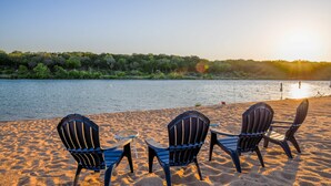 Une plage avec trois chaises Adirondack et une table, donnant sur une rivière bordée d’arbres.