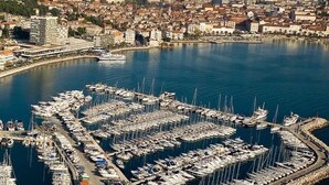 An aerial view of a marina with numerous boats docked, surrounded by a coastal cityscape with buildings and mountains in the background. - d - Beautiful Studio in the Heart of Split (Split)
