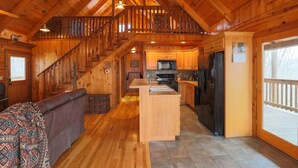 A spacious log cabin interior with a wooden staircase, a kitchen with modern appliances, and a cozy seating area. - Rustic Retreat 2 BD/1 BA cabin near Pigeon Forge (Sevierville)