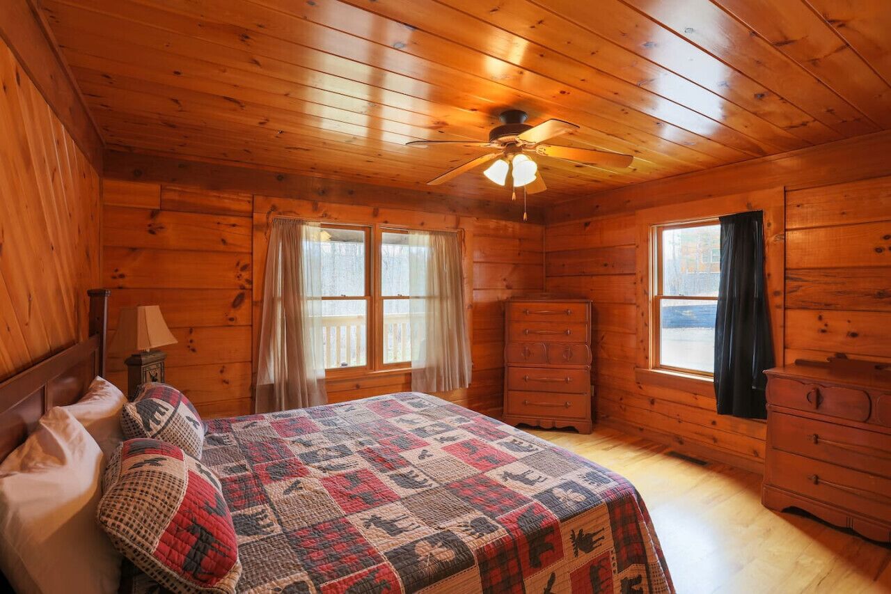 A cozy wooden cabin bedroom with a bed, dresser, and a ceiling fan.