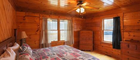A cozy wooden cabin bedroom with a bed, dresser, and a ceiling fan.