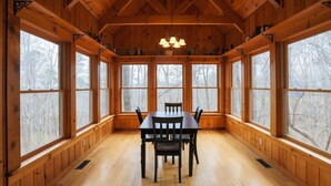 A wooden-paneled room with a table and chairs, large windows, and a chandelier. - Rustic Retreat 2 BD/1 BA cabin near Pigeon Forge (Sevierville)