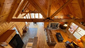 A spacious loft-style living area with a high ceiling, wooden beams, a fireplace, and large windows. - Rustic Retreat 2 BD/1 BA cabin near Pigeon Forge (Sevierville)