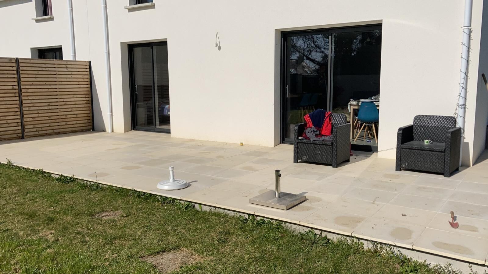 Un patio con suelo de baldosas, mobiliario exterior y una puerta corrediza de vidrio que da a un espacio interior.